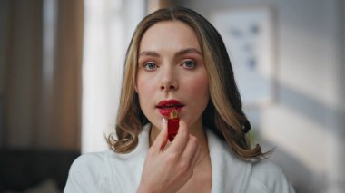 Sabah hanımı otel portresine bakarak dudak boyuyor. Açık renkli dairede elinde pahalı ruj tutan zengin bakımlı bir kadın. Beyaz bornozlu sakin manken içeride makyajın keyfini çıkarıyor.