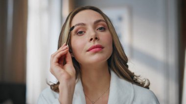 Pov modeli evde kaş şekillendirici ayna yansıması yapıyor. Tatmin olmuş kız kameraya poz veriyor. Daireye yakın çekim yapıyor. Gülümseyen kadın kaşlarını tarıyor makyaj resmi hazırlıyor.