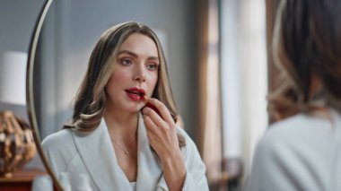 Sabahları elinde ruj tutan, dudak boyayan lüks bir kadın. Yansımasına gülümseyen muhteşem bir kadın randevuya hazırlanıyor. Makyaj yapan tatmin olmuş bir model.