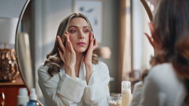 Kapalı alanda aynaya dokunan güzel bir bayan. Genç bir kadın tuvalette yüz masajı yapıyor. Odaklanmış model jimnastik egzersizleri yapıyor. Ev konseptinde güzellik hizmetleri