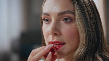 Evdeki iş kadını dudaklarını boyuyor. Zengin, bakımlı, elinde pahalı ruj tutan bir kadın. Işıklı dairede yansımasına gülümsüyor. Mutlu pozitif kız sabah makyajını evde yapıyor.
