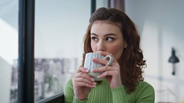 Kahve fincanı tutan esmer, ofis penceresinden şehir manzaralı. Çekici, gevşemiş, iş başarısı düşünen bir kadın. Meşrubat içen muhteşem iş kadını. Cappuccino içen kadın. 