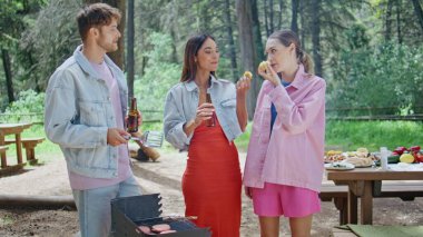 Barbeküde konuşan üç arkadaş orman pikniğinde ızgara yemek yiyorlar. Güzel yeşil parkta bira içen mutlu iş arkadaşları. Rahatlamış gençler BBC 'nin güneşli doğada toplanmasının tadını çıkarıyorlar..