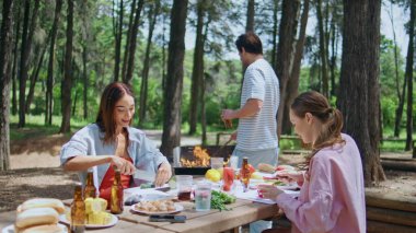 Grup üyeleri güzel güneşli parkta bbq hazırlıyorlar. Gülümseyen kadınlar salata için sebze kesiyorlar. Rahatlamış bir adam, elinde soğuk birayla ateşte yemek pişiriyor. Mutlu genç arkadaşlar ormanda barbekü partisinin tadını çıkarın.