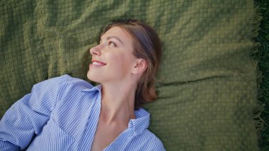 Gülümseyen bayan, neşeli bir ifadeyle doğanın üzerine uzanıyor. Kaygısız çekici kadın piknik battaniyesinde neşe ve memnuniyet sergiliyor. Yaz parkında yeşil çimlerde rahatlayan esmer portresi..