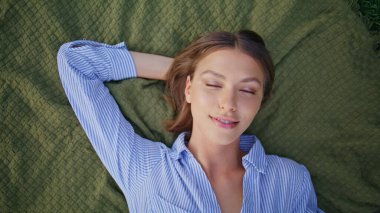 Yeşil çimlerin üzerinde uzanan güzel bir model, sakin bir yüz ifadesi var. Yakından kumral bir kadın kameraya bakıyor ve güzel doğayı seyrediyor. Rahatlamış bir kızın portresi gülümseyerek huzurlu anın tadını çıkarıyor..