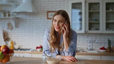Konuşan bir kadın akıllı telefon tutuyor ve evde sabahları eğleniyor. Modern mutfakta cep telefonuyla konuşan sarışın güzel bir kızın portresi. Mutlu rahat ev hanımı cep telefonuyla iletişim kuruyor. 