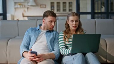 Eşler rahat oturma odasında oturan aletleri konuşuyor. Gülümseyen eş, yerde rahat genç kocaya dizüstü bilgisayar ekranı gösteriyor. Mutlu evli çift hafta sonu online alışverişi tartışıyor. 