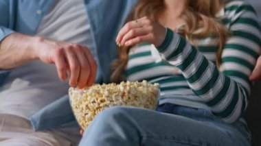 Evdeki cam kaseden patlamış mısır alan iki el. Kaygısız kadın aşıklar hafta sonları birlikte televizyon izliyorlar. Rahat eşler komedi filminin keyfini çıkarıyorlar düz koltukta rahat bir şekilde oturuyorlar 
