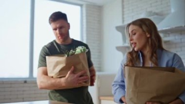 Beyaz mutfak iç kısmında kağıt poşetler taşıyan mutlu bir kadın. Aile çifti, sağlıklı yiyeceklerle birlikte yiyecek paketlerini boşaltıyor. Modern dairede ev işlerini paylaşan sevimli bir çift.