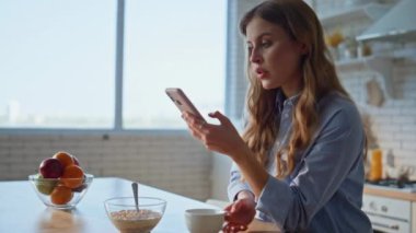 Cep telefonlu bir kadın apartmanın mutfağında kahve içiyor. Portre çekici, rahat kadın hafta sonu akıllı telefon uygulamasına göz atıyor. Evcil kız sabah içeceği görünümlü telefondan hoşlanır. 