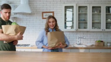 Eşler marketten geldi ve mutfak masasını kapattılar. Gülümseyen aile, ev mutfağında eko-kağıt paketleri açıyor. Yemek pişirmek için tezgahta yemek sıralayan mutlu çift. 