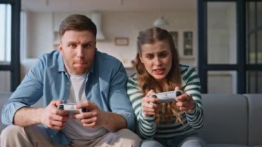Çevrimiçi rekabet konsolları tutan bir çift. Hayal kırıklığına uğramış kadın oyuncu odada video oyunu kaybediyor. Üzgün erkek arkadaş kazananı başarıya seviniyor. Oyuncular video oyunları oynuyorlar.