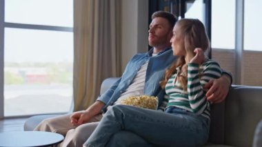 İki izleyici TV 'de eğlenceli bir film izliyor rahat bir apartman kanepede yakın çekim. Gülümseyen çift evde patlamış mısır ve televizyonla rahat vakit geçiriyor. Rahat bir çift kanepe üzerinde eğlence programının keyfini çıkarın. 