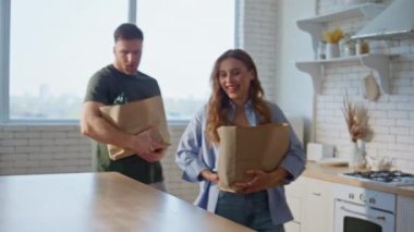 Aile çifti, beyaz mutfak iç kısımlarında yiyecek paketlerini boşaltıyorlar. Sağlıklı yiyeceklerle dolu kese kağıdı taşıyan mutlu bir kadın. Modern dairede ev işlerini paylaşan sevimli bir çift.