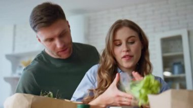 Eşler, daire mutfağında kağıt paketlerinden ürünleri alıyorlar. Yakın plan mutlu aile çiftleri organik yiyecekleri ekolojik poşetlere boşaltıyor. Ev idaresi konseptinde ortaklık
