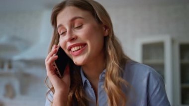 Kapanış konuşması yapan akıllı telefonlu kadın evde eğleniyor. Duygusal gülümseyen güzel kız elinde cep telefonu, modern mutfakta duruyor. Mutlu, rahat ev hanımı cep telefonuyla iletişim kuruyor.