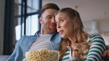 Harika bir çift TV 'de eğlenceli bir film izliyor rahat bir apartman kanepede yakın çekim. İki izleyici evde patlamış mısır ve televizyonla rahat vakit geçiriyor. Gülen çift kanepede eğlence programının keyfini çıkarın. 