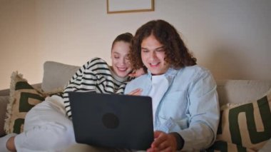 Oturma odasındaki rahat koltukta dizüstü bilgisayardan film izlemeyi seçen gülümseyen çift. Mutlu eşler akşam kanepesinde bilgisayara bakıyorlar. Neşeli çift kablosuz teknolojiyle huzur içinde dinleniyor.