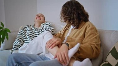 Oyuncu koca, karısının bacaklarını gıdıklıyor. Daire kanepesinde yan yana rahatlıyor. Mutlu kadın gülüyor, evde kıvırcık saçlı adamla eğleniyor. Neşeli romantik çift kanepenin keyfini çıkarın..