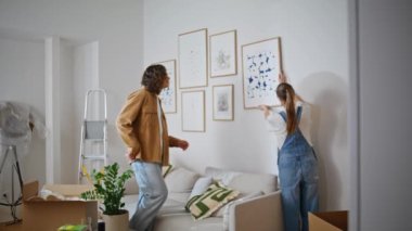 Birlikte resim asarak evi dekore eden aile çifti. Modern oturma odasının duvarına resim çizmek için işbirliği yapan mutlu kadın. Genç eşler modern apartman alanı yaratıyor.