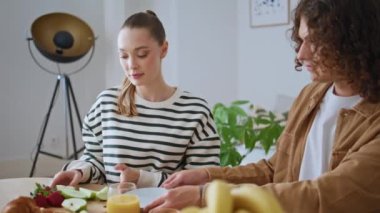 Çift mutfak masasında aile kahvaltısının tadını çıkarıyor. İki sevgi dolu insan, hafif dairede sağlıklı taze yiyecekler yemeye hazırlanıyor. Güzel kız arkadaş sabah evde sevgili erkek arkadaşıyla konuşuyor..