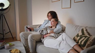 Sakin eşler, modern akşam evinde dinlenirken televizyonu açıyorlar. Tasasız evli çift, televizyon programı izlerken rahat koltukta oturuyor. Rahatlamış ruh eşleri kanepede romantik bir şekilde eğleniyorlar.