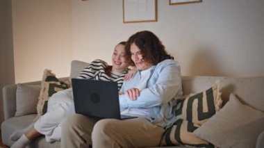 Eşler, akşam rahat oturma odasındaki kanepede oturan arkadaşlarıyla video görüşmesinden hoşlanırlar. Dizüstü bilgisayarla konuşan, kanepede dinlenen gülümseyen genç çift. Mutlu ruh eşleri bilgisayarla iletişim kuruyor.