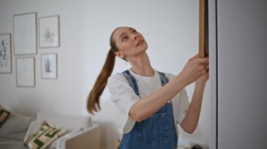 Duvara resim asarak duvar dekore eden genç bir kadın. Mutlu eş, kocasının fikrini soruyor. Yeni bir dairede resim tutuyor. Gülümseyen kız estetik yaşam alanı kurarak yaratıcı bir işe girişiyor.