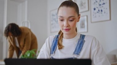 Karısı, şık bir odada dizüstü bilgisayarda çalışıyormuş. Kocası arka plandaki modern daireyi toparlamakla meşgul. Ciddi bir kadın bilgisayar ekranına bakıyor ve online alışverişleri seçiyor. Aile yaşam tarzı konsepti.