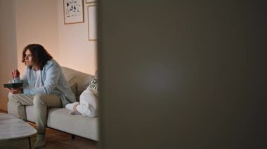 Eşler hafta sonunu dairede rahat kanepe manzarasında ayrı ayrı oturarak geçirirler. Ciddi bir adam televizyon izlerken abur cubur yiyor. Üzgün kadın, koltukta gergin bir ifadeyle akıllı telefona bakıyor..