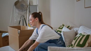 Yeni evinizde kutuları açan genç bir kadın düşünceli hissediyor. Ciddi bir apartman sahibi kanepe oturma odasında oturmuş karton paketten kitaplar alıyor. Evin içinde rahat ve rahat hisseden bir bayan..