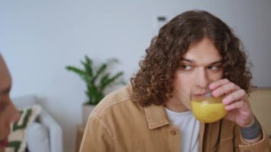 Rahatlamış erkek arkadaş meyve suyu içiyor ve mutfaktaki mutlu kız arkadaşla konuşuyor. Turuncu içecekten zevk alan gülümseyen adam sevgili karısına evde bakıyor. Adam aile kahvaltısında ferahlatıcı.