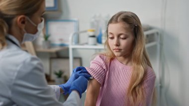 Doktor, tıbbi tesiste çocuk enjeksiyonu yapıyor. Aşı aşısı için kliniğe gelen tatlı bir kız. Maskeli sağlık uzmanı hastanede şırıngayla steril işlem yapıyor..