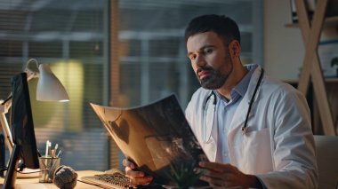 Geceleri röntgeni yakından inceleyen mutlu bir terapist. Gülümseyen doktor, radyografiyi kontrol et. Akşamları işe yarıyor. Klinikteki teşhisi analiz eden sağlık uzmanı..