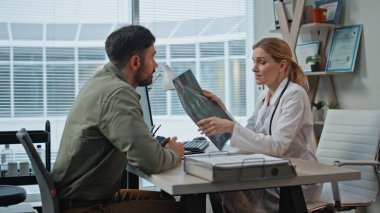 Klinikteki muayene sırasında röntgen hastasını gösteren doktor. Gülümseyen doktor, mutlu adamın Buro 'da başarılı tedavi sonuçlarını tartıştığını söylüyor. Neşeli insanlar el sıkışıyor rehabilitasyondan sonra taramanın tadını çıkarıyor