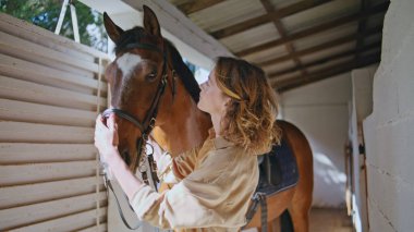 Atlı at çiftliği otlağını okşayan kadın. Çiftlikte mutlu dişi kovboy bağlanma aygırı ağza dokunuyor. Kamera önünde poz veren bir model. Kadın evcil hayvan arkadaşlığı. Binicilik konsepti