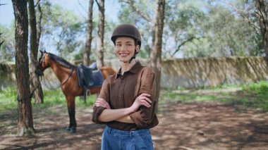 Açık havada mutlu kadın jokey portresi. Otlakta duran güzel kısrak. Kasklı gülen biniciler yaz manzarasında poz verirken kameraya bakıyor. Hayvanları eğitmek at koşusu sporu konsepti