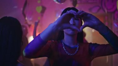 Mutlu kız parti klubü sevgi ve yakınlığı ifade eden kalp jestleri yapıyor. Festivalde gece kulübünde dans eden Asyalı bir kadın. Enerjik kulüp üyesi neon kulüpleme ortamından zevk alır.