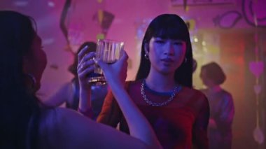 Coşkulu bir kulüpte kokteyl bardağı tutan bir kadın. Pembe neon ışıkta dans eden kaygısız Çinli kız. Modern gece kulübünde arkadaşlarıyla dans eden hippi bir kadının portresi..