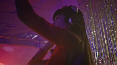 Disko klübü kapanışında dans eden bir jokey, müzik karıştırıyor kulaklıkla müzik dinliyor. Gece kulübü performansı sırasında mutlu Asyalı kadın DJ kontrol ekipmanları. Enerjik ve hareketli bir gece kulübü.