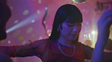 Canlı bir gece kulübünde dans eden Asyalı kadın. Kaygısız esmer, kırmızı elbiseli, hareketli vücudu olan, disko barında mutluluğu hisseden. Parlak makyajlı mutlu kız hafta sonu eğlencesinin tadını çıkar.