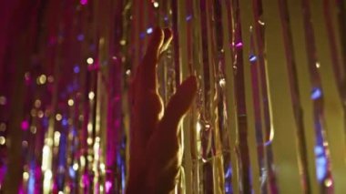 Eller parti dekorasyonlarıyla oynuyor. Yakın plan. Tanınmayan kulüp üyesi, canlı bir gece kulübünde ışıltılı bir dekora dokunuyor. Nazik kadın parmakları, neon lambalarda parıldayan striptizcilere dokunuyor.. 