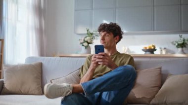 Gülümseyen adam rahat koltukta cep telefonu ekranına bakıyor. Cep telefonuyla mesajlaşan mutlu genç adam koltukta oturuyor. Evde oturma odasındaki akıllı telefondan mesai mesajı atan rahat bir işçi. 