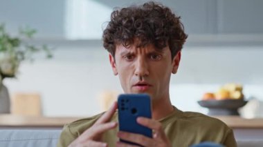 Hüsrana uğramış bir adam aydınlık ev oturma odasında akıllı telefon mesajı okuyor. Memnuniyetsiz adam evdeki koltukta cep telefonuyla mesajlaşırken gergin tepki veriyor. Endişeli iş adamı koltukta cep telefonu ekranı görüyor.