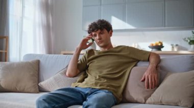 Modern oturma odasındaki sorunlara üzülen adam. Ciddi genç adam televizyon şovuna odaklanmış rahat koltukta tek başına oturuyor. Endişeli esmer hafta sonları televizyon seyrediyor. 