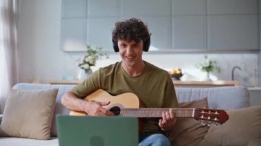 Oturma odasında gitar çalan mutlu bir müzisyen. Gülümseyen adam evde dizüstü bilgisayar kullanarak müzik dersi kaydediyor. Olumlu gitarist dairede telli çalgılar çalarken kafasını hareket ettiriyor. Hobi konsepti 