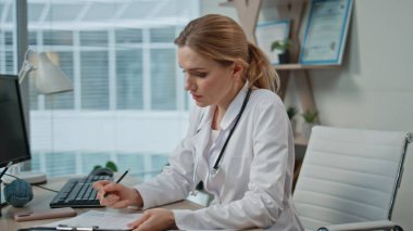 Tıbbi muayene sırasında danışman doktor not alıyor. Kapalı hamile kadın sağlık görevlisiyle semptomları tartışıyor. Sigorta randevusu sırasında odaklanmış profesyonel dinleme hastası.