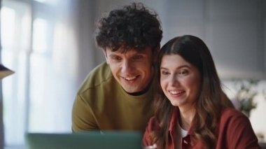 Ev sahibi çift modern oturma odasında dizüstü bilgisayara bakıyor. Harika bir kadın, bir erkekle internette masa alışverişi yapıyor. Olumlu gülen genç ortaklar satın almayı tartışıyor dairede eğleniyorlar. 