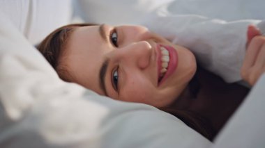 Kapalı yerde, battaniyenin altında, rahat bir yatakta uzanmış mutlu bir şekilde yakın çekim yapıyor. Gülümseyen kadın rahat beyaz yatak odası kamerasında dinleniyor. Neşeli esmer, rahat yatak odasında evcil sabahın tadını çıkarıyor..